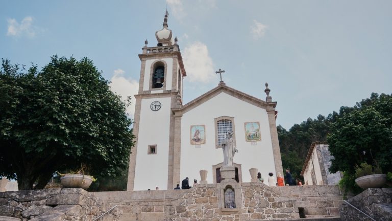 Igreja minhota vista de baixo, com a torre sineira e uma árvore em primeiro plano