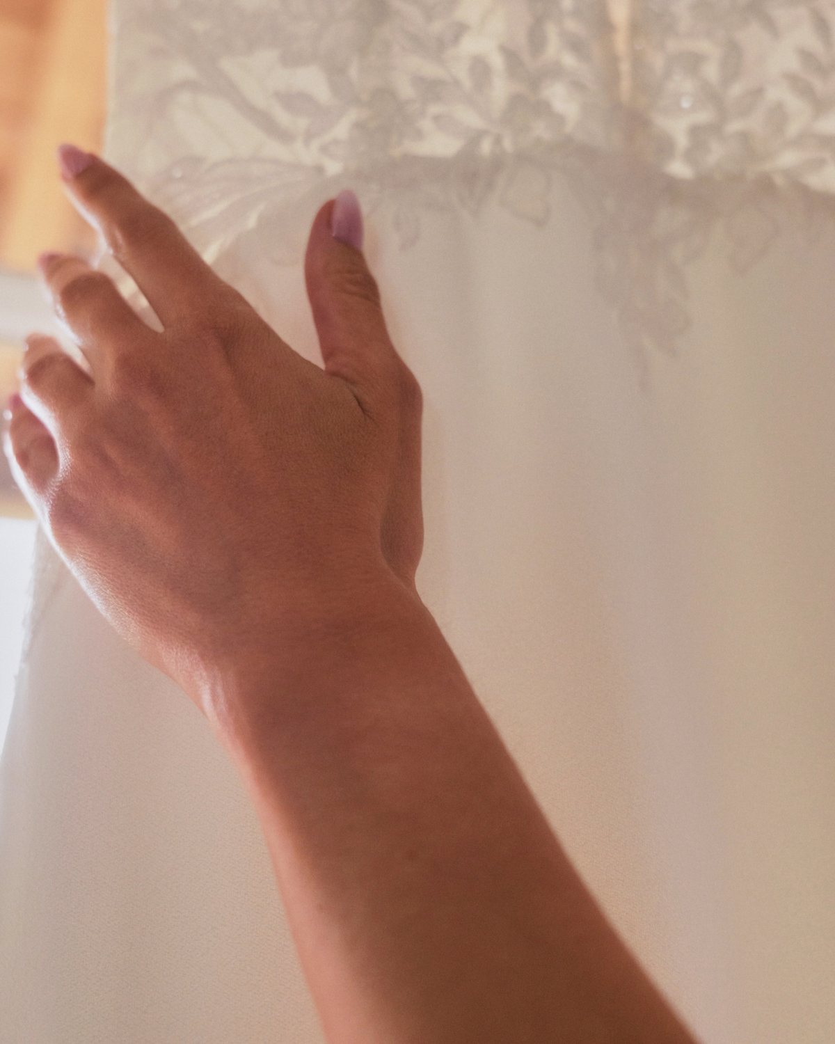 Mão a tocar no vestido pendurado contra a janela